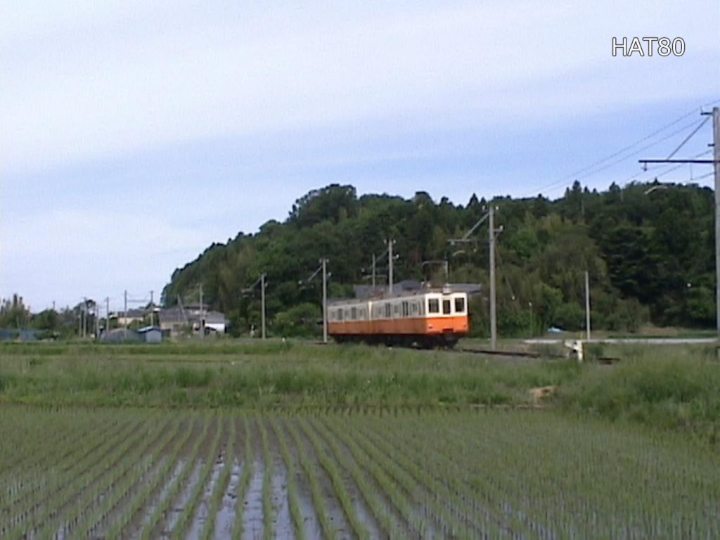 青空の下、水田に姿を映して電鉄が行き交う。 川中子から太田方面へ向かう緩くカーブした場所は、林を背景に民家と水田の境界を縫って走るローカルな雰囲気が気に入り、その後何度も訪れることになった。